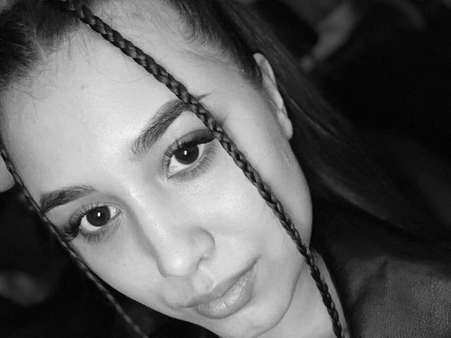 ShawneeLinderholm's face, black and white, with braided hair in front, full eyebrows, long eyelashes, subtle smile, and smooth skin. Boobs not visible, focus on facial features.