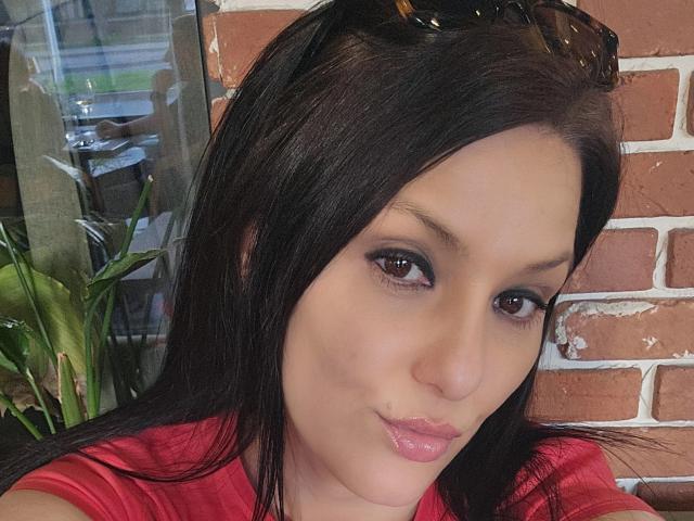 JoliDanielle tiene el pelo negro, ojos marrones y lápiz labial rosa. Lleva una camisa roja y tiene gafas de sol en la cabeza, mostrando un gesto lindo. Sus pechos son ligeramente visibles..