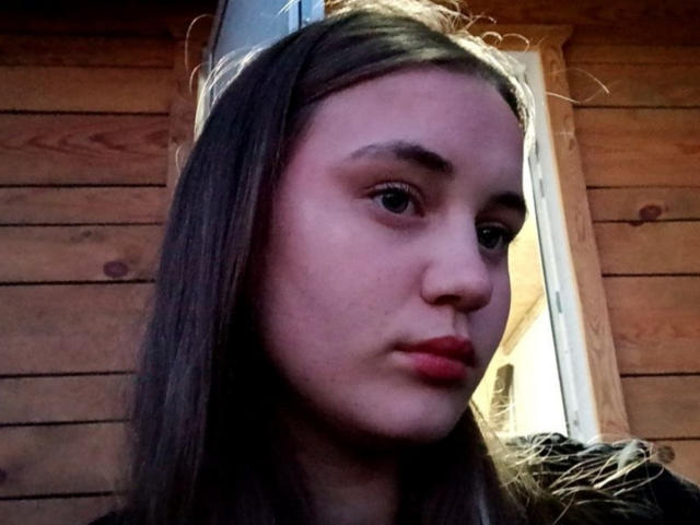 AlysiaFinkelstein has light brown skin, straight brown hair, and red lipstick. She's looking to the side with a neutral expression. Her ass is not visible.