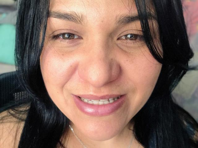 VivianaThompson has black hair, brown eyes, and a nose piercing with a small ring. Her pink lips are slightly parted, showing her teeth. She's smiling softly.