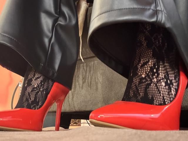 HannaBorbon's black lace stockings and shiny red stiletto heels with tall red heels, showing her legs in black leather pants. Her ass is partially visible.
