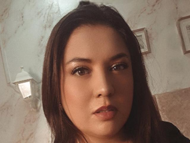 PaulaAnd has medium brown skin, dark brown hair, and brown eyes. She's making a slight pouty face with her lips slightly parted. Her nose is small and cute.
