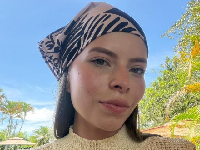 AnnaFer with a zebra-pattern headscarf, has a cute face, small nose, and pink lips, wearing a beige knit sweater, looking at the camera with a slight smile.