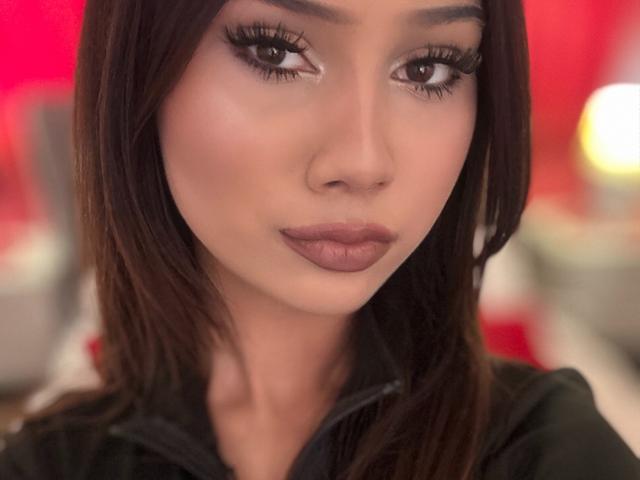 VelvetKisse has medium brown skin, long dark brown hair, and full lips with mauve lipstick. Her eyes are brown with thick black eyelashes, and she's wearing a black top.