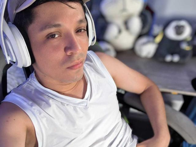 LukaForge, a medium-skinned dude with short dark hair, wearing white headphones and a sleeveless white shirt, looking slightly bored. His ass is slightly visible under the shirt.