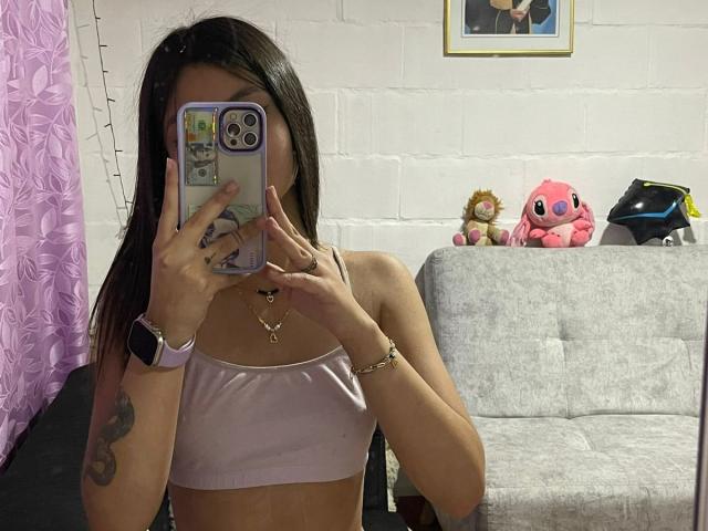 ScarlettPreatty taking a mirror selfie, wearing a pink sports bra, showing her tits, holding a phone with a colorful case, wearing a smartwatch, and a bracelet.