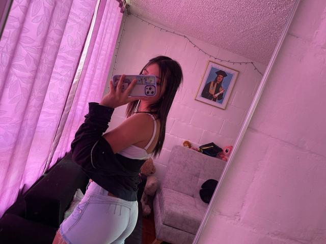ScarlettPreatty with medium ass, wearing white bra and tight light blue jeans, black jacket off, mirror selfie, purple curtains, holding phone with purple case, white wall, small painting.
