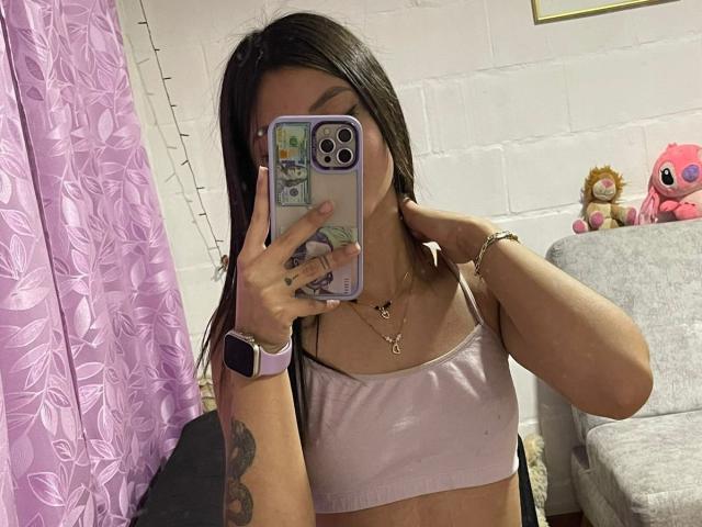 ScarlettPreatty taking a mirror selfie with her phone, covering her face, wearing a pink sports bra, long dark hair, tattoo on her arm, and a wristwatch.