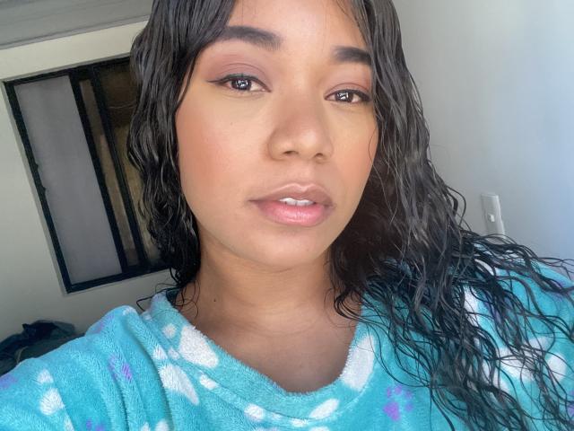 AvaJones69 with wet black hair, brown eyes, and pink lips, wearing a blue floral robe, has a cute face and small, cute tits. She's looking at the camera.