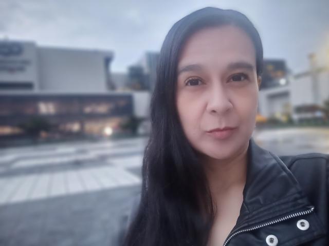 AileenRamirezW with long black hair, light skin, and a slight smile, wearing a black leather jacket, looking at the camera with a relaxed, slightly curious expression.