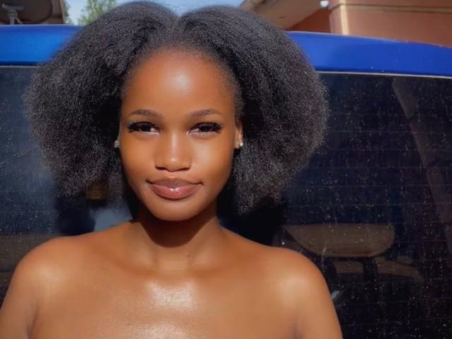PieretteE has dark, fluffy afro and smooth brown skin with a subtle smile. She's topless, showing her bare shoulders and small, round, shiny earrings. Her ass is not visible.