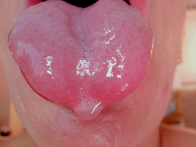 EmiliaMilf's pink, glistening tongue is hanging out, wet and slightly foamy, with a shiny, reflective surface. Her tongue is centered, filling most of the frame.
