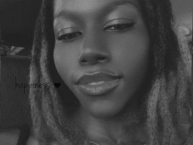 KharlaQueen's face with dark skin, medium-length dreadlocks, subtle eyeliner, and glossy lips, smiling slightly. Her nose is small, and she has a cute, sexy look.