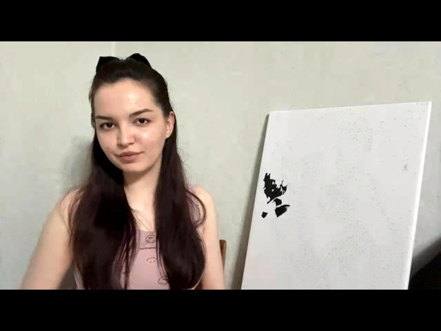 SandraRebar has long dark brown hair, wearing a pink sleeveless top, standing with a white canvas featuring black abstract shapes in the background.