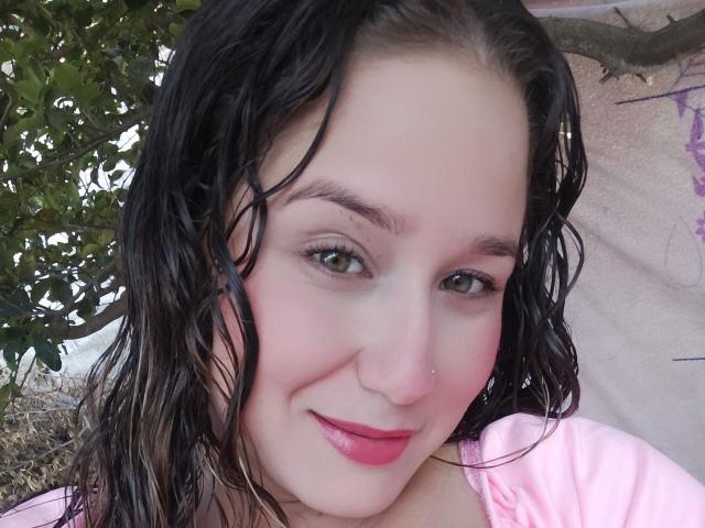 AlexaHotSeins has wet black hair, green eyes, pink lipstick, and a nose ring. She's wearing a pink shirt, smiling with pink cheeks, and has a small nose piercing.
