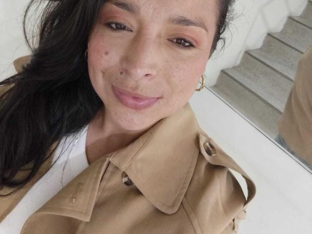 StangelarRivera has a cute smile with a small mole on her left cheek, brown eyes, and long black hair. She wears a tan jacket over a white top.