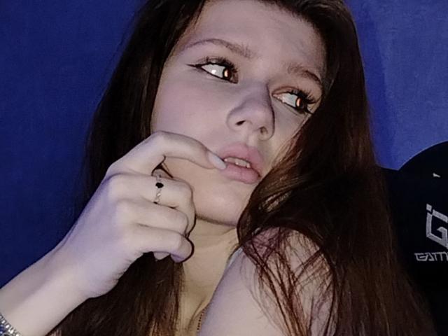 Kary Whitler, avec ses longs cheveux bruns, touchant son menton avec une bague à l'annulaire, regardant sur le côté avec les yeux à moitié fermés, dans un environnement éclairé en bleu..