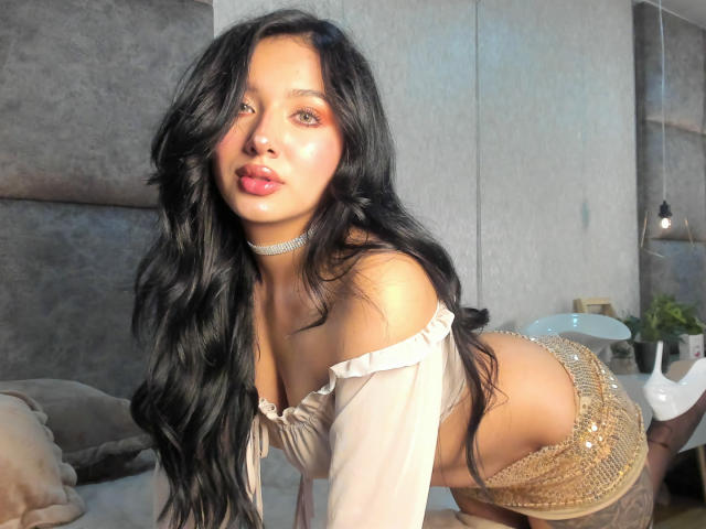 LillyTaylor with long black hair, pouty red lips, off-shoulder top, gold sequined shorts, choker, on all fours, showing her tits and ass, in a sunlit room.