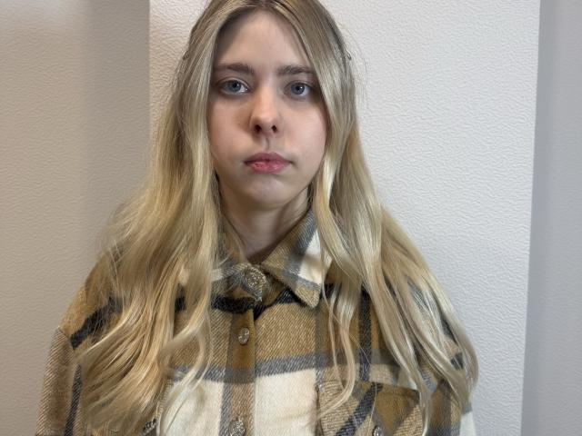 JennyMontelle with blonde hair, wearing a beige and brown plaid shirt, has a neutral expression and small pink lips. Her ass is not visible.