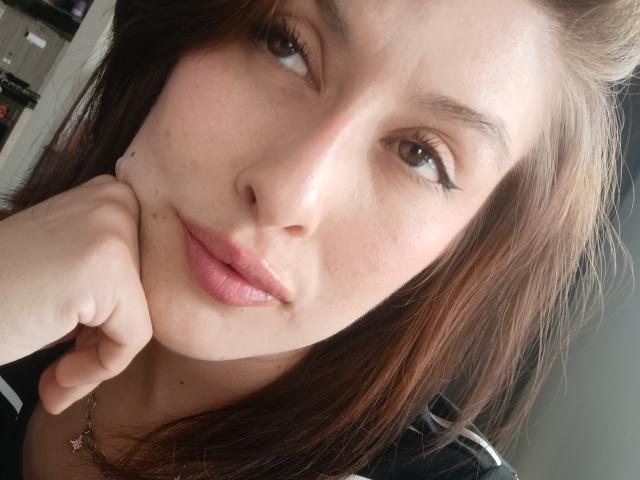 IsabellaPalacio's face, brown eyes, black eyeliner, pink lips, hand under chin, brown hair, slight smile, fair skin, small beauty mark near nose, black and white shirt.
