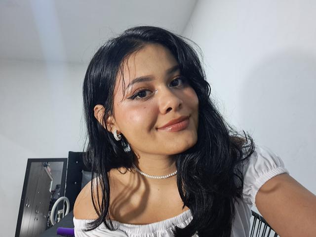 JennLunaLee tiene el pelo largo y negro, ojos marrones y una ligera sonrisa. Lleva una blusa blanca con un hombro descubierto y un collar de perlas. Sus pechos son pequeños y es muy linda..