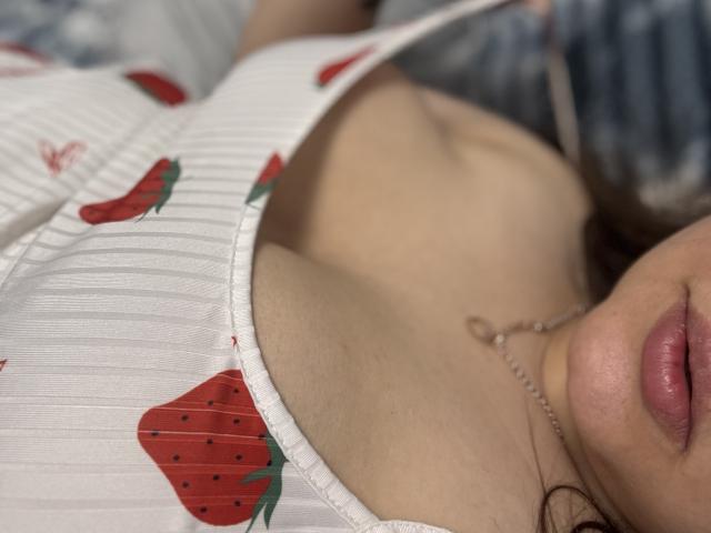 AngiieHot's white dress with strawberry prints, showing her cleavage and small, round tits. Her pink lips and silver necklace are visible. Her skin is light.