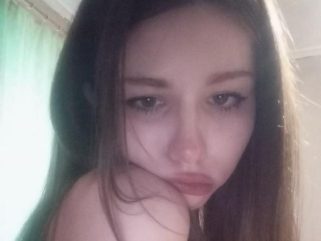 EileneSzala with long brown hair, pouty lips, and half-closed eyes, staring at the camera, her bare shoulder visible, looking slightly sad. Her tits are partially out of frame.