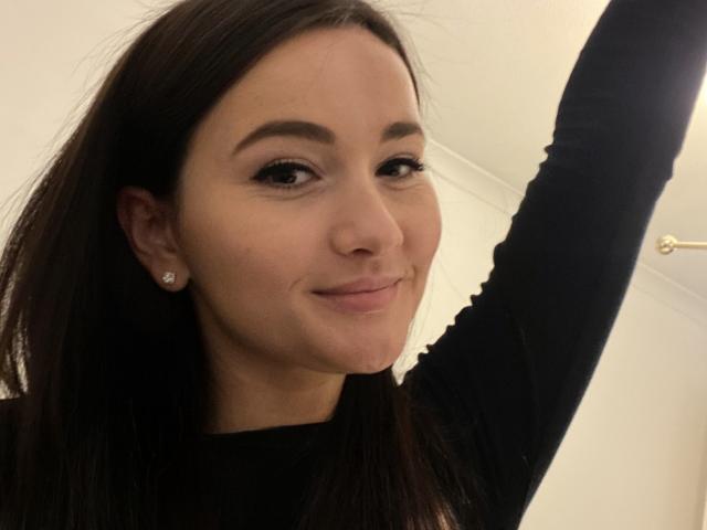 Dionisia a de longs cheveux bruns foncés, un trait d'eye-liner noir, et un léger sourire. Elle porte une chemise noire à manches longues, lève son bras droit et montre de petites boucles d'oreilles en diamant..