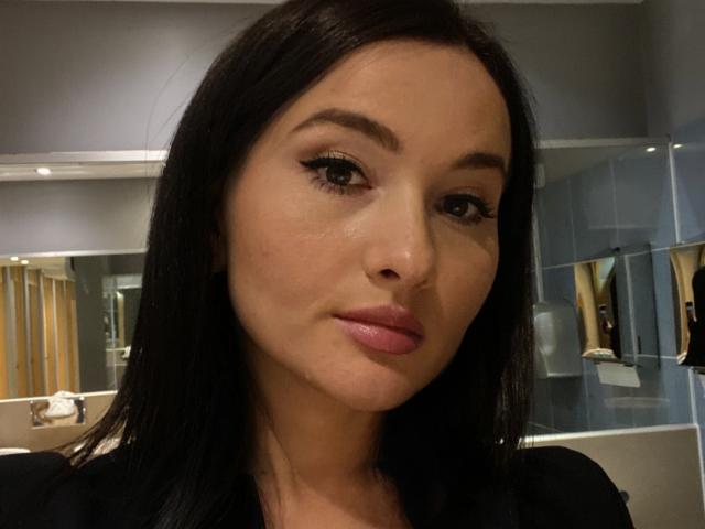 Dionisia has dark straight hair, brown eyebrows, long eyelashes, pink lips, and a slightly smiling face with a smooth, fair complexion in this selfie.
