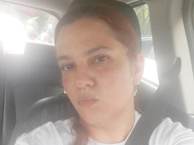 AmeliaWilson has light brown skin, small tits, and brown eyes, wearing a white shirt with red marks on her cheek, sitting in a car with a seatbelt.
