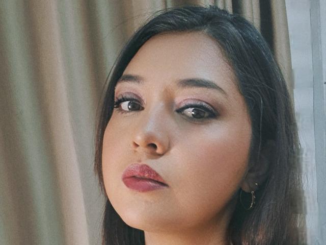 PaulaAnd has tan skin, dark brown eyes, pink eyeshadow, and pink lipstick. She's wearing black earrings and has straight black hair. Her face is centered in the shot.