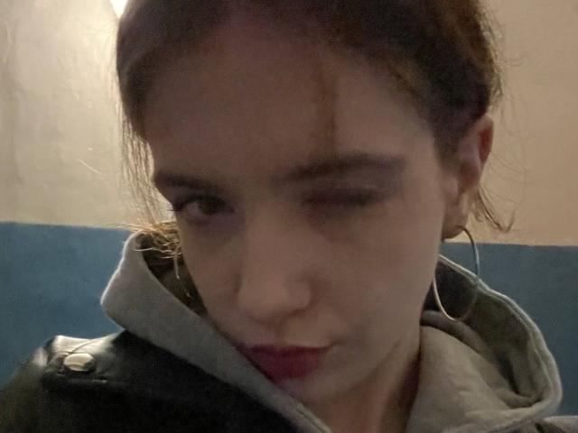 EviaMarcot has a pained expression, slightly squinting eyes, and a small cut on her upper lip. She's wearing a gray hoodie with black leather shoulders.