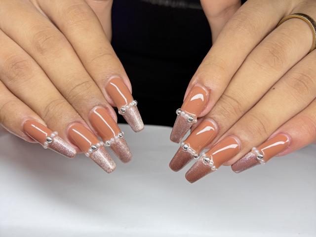 SofiaCumness's hands with sparkly pink and white nail polish, long glittery nails, and silver beads between each nail. She's wearing a black top and a gold bracelet.