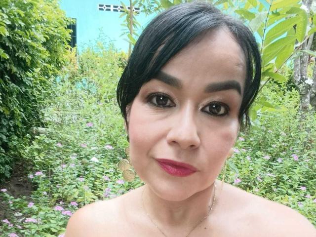 TamaraFoxy has short black hair, dark eyebrows, and pink lipstick. She's topless with a subtle necklace, and has a slightly chubby, cute face and brown eyes.