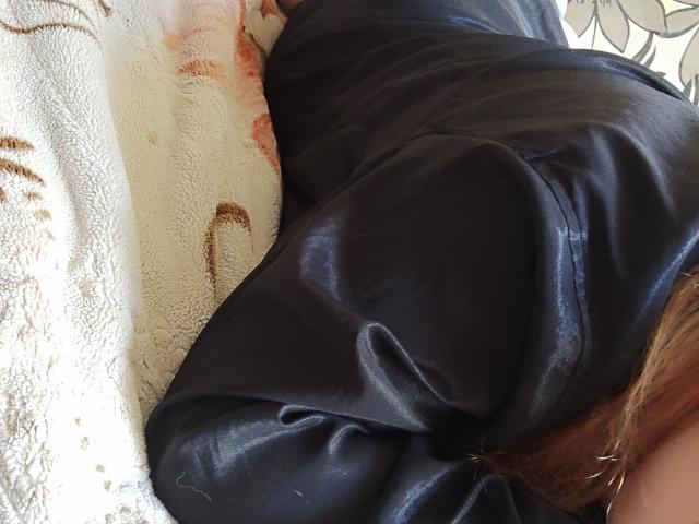 MinistraX's black leather-covered ass is prominently displayed, lying on a white, floral-patterned blanket with her brown hair partially visible on the right side of the image.