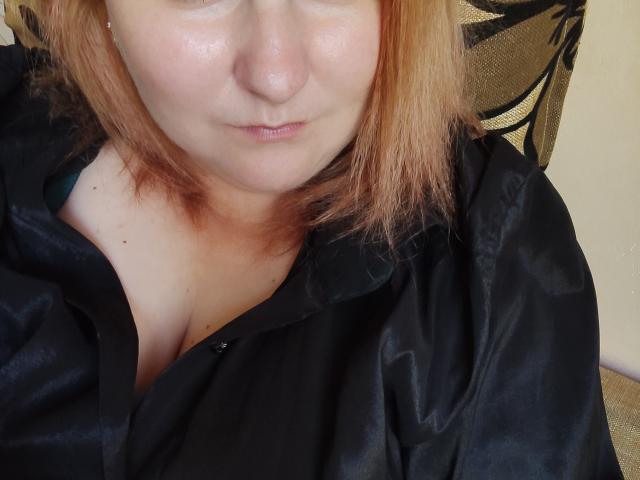 MinistraX with pale skin and pinkish-brown hair, wearing a black shirt, exposing her tits, slightly parted lips, and a small nose piercing, in a relaxed, close-up shot.
