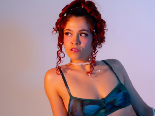 ArielleBrooks with red curly hair, green camo bra, pearl necklace, looking to the side, light blue and orange lighting, subtle blush, wet skin on chest, small tits, sexy.