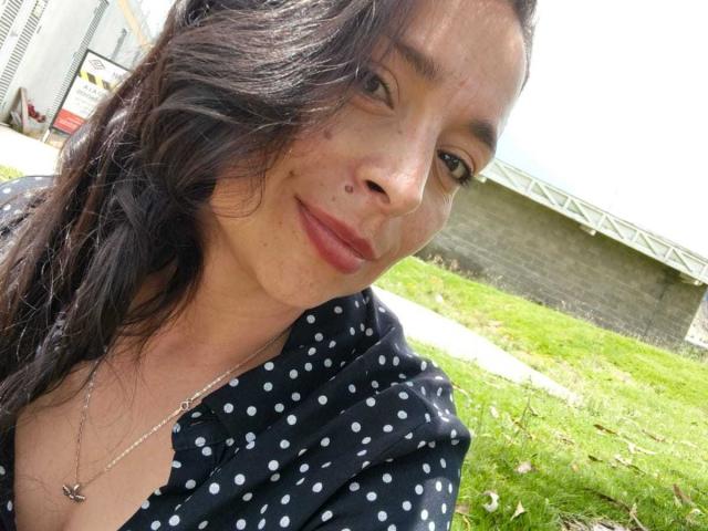 StangelarRivera with brown hair, wearing a black polka dot shirt, has a small mole on her left cheek, and is smiling with her lips slightly closed, wearing a necklace.