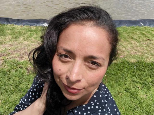 StangelarRivera has a cute face with medium brown skin, black wavy hair, small nose, and brown eyes. She's wearing a polka dot shirt, sitting on green grass.