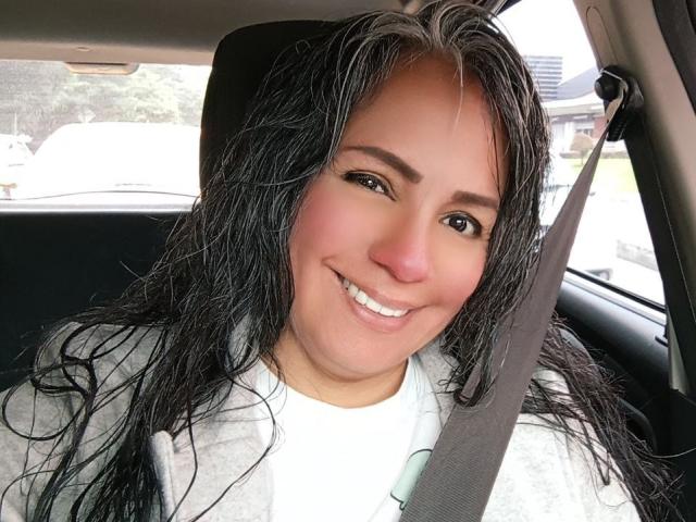 LailaCastillo has wet black hair, a cute smile, and is wearing a seatbelt in a car, with her tits barely visible under a gray hoodie.