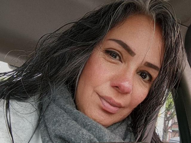 LailaCastillo has wet black hair, brown eyes, and a slight smile, wearing a gray scarf, with a light skin tone and a cute face, looking at the camera.