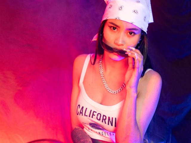 KarolPalacios with a white bandana, chain necklace, and white tank top, smoking a joint, has tattoos on arms, and a sexy, slim figure with small tits. Red and purple lighting.