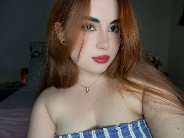 VicluX has pale skin, red hair, and wears a strapless blue and white top, showing her bare shoulders and small tits. She's wearing a necklace with a heart pendant.