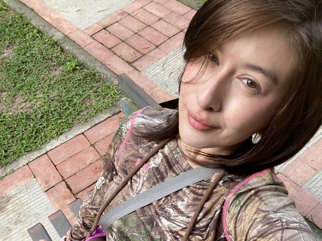 IsabellaPalacio with brown hair, wearing a camo hoodie, has a seatbelt across her chest, and is smiling at the camera, showing her small tits.