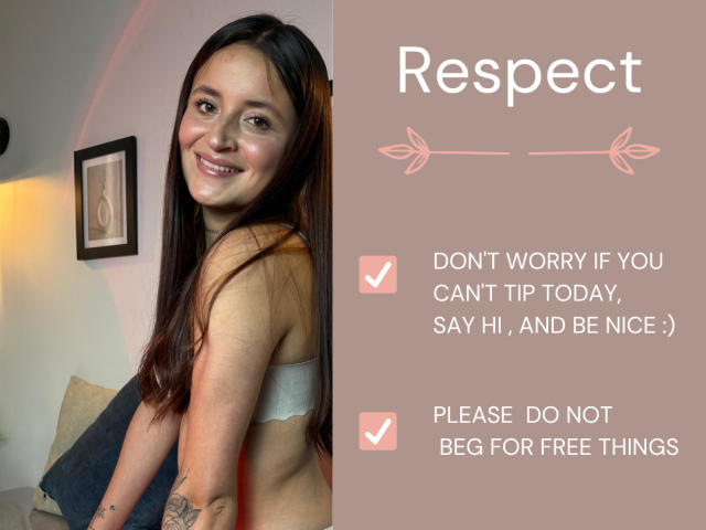 LucyArcy with long brown hair, smiling, wearing a gray bra, showing her tits and a tattoo on her arm, in a soft-lit room. Text on right: "Respect".