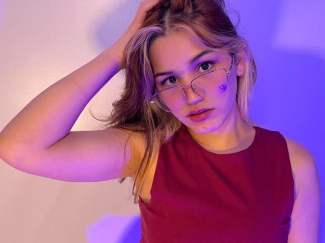 ElodieGardner with glasses, red sleeveless dress, blonde hair, hand in hair, blue and purple lighting, small nose piercing, slightly parted lips, looking at camera.