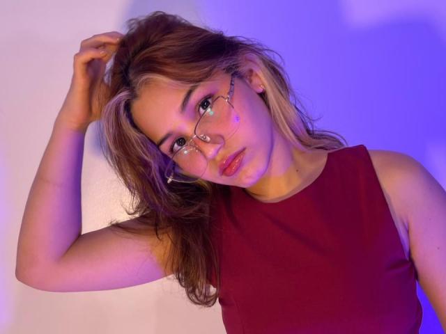 ElodieGardner with glasses, red sleeveless top, brown hair, and pink lips, hand in hair, blue-purple light, looking slightly to the side, soft expression, slight blush.