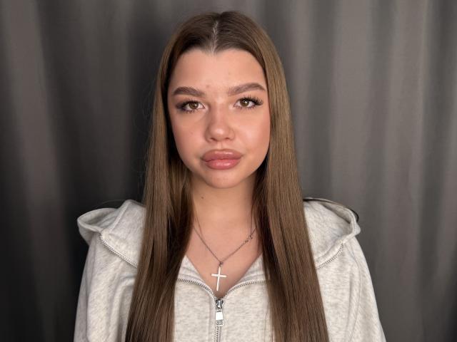KristieShofestall tiene el pelo largo y castaño, ojos marrones y labios gruesos y rosados. Lleva una sudadera gris con un collar de cruz. Su rostro está ligeramente enrojecido..