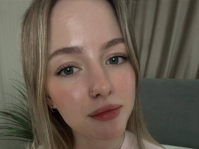 AlbertinaOberer's face, with light green eyes, blonde hair, nose ring, and pink lips, shows a slight smile, and has a subtle blush on her fair skin.