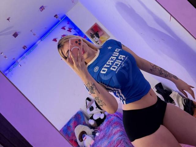 SammyViolet with blonde hair, blue Chelsea FC shirt, black shorts, tattoos, holding phone in mirror, showing her tits and ass. Reflection, bedroom, blue lights, stuffed animals.